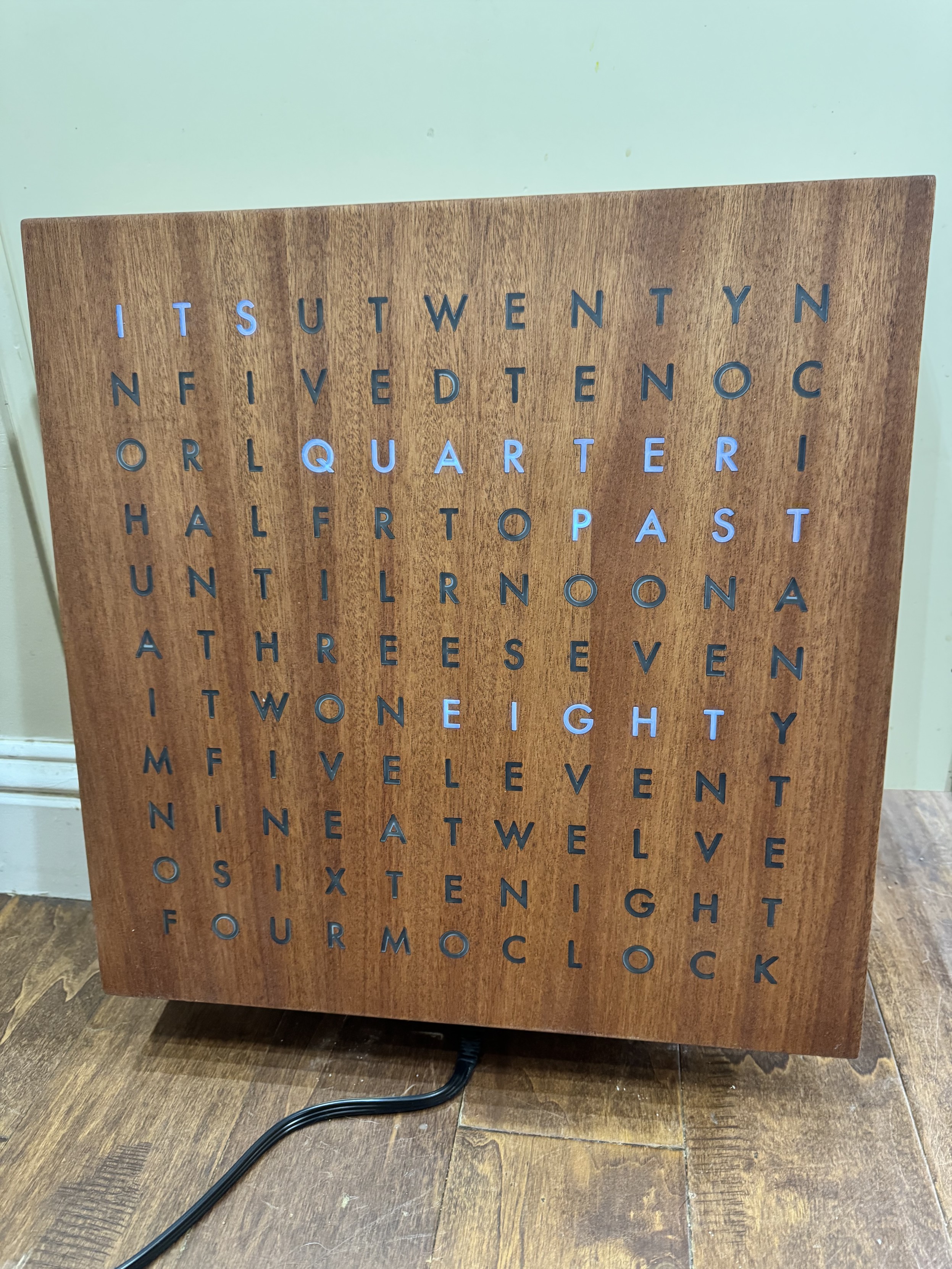 Wooden clock made from fixed individual letters that show the current time. “ITS QUARTER PAST EIGHT” currently lit up.